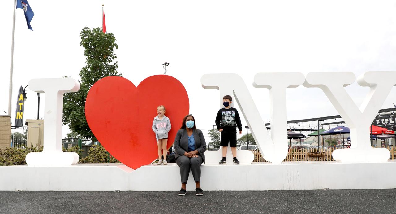 Attorney General James sitting on I love New York sign with two children