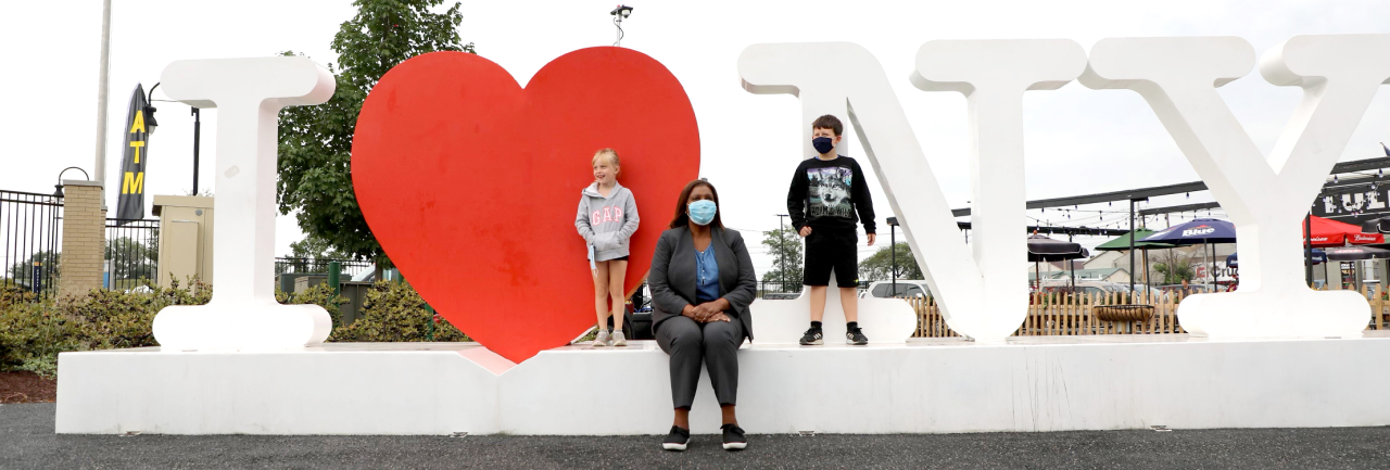 AG James sitting on I love New York sign with kids